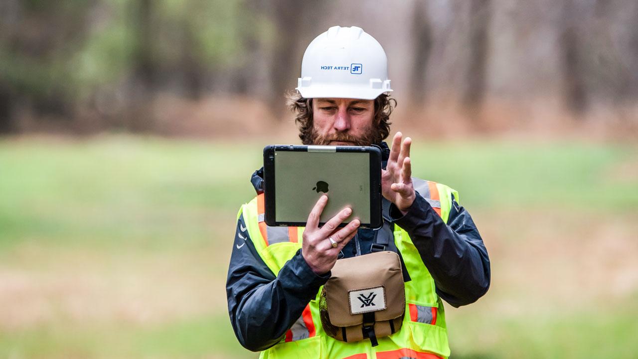 Worker wearing safety gear using a tablet to collect location, habitat data, and photographs